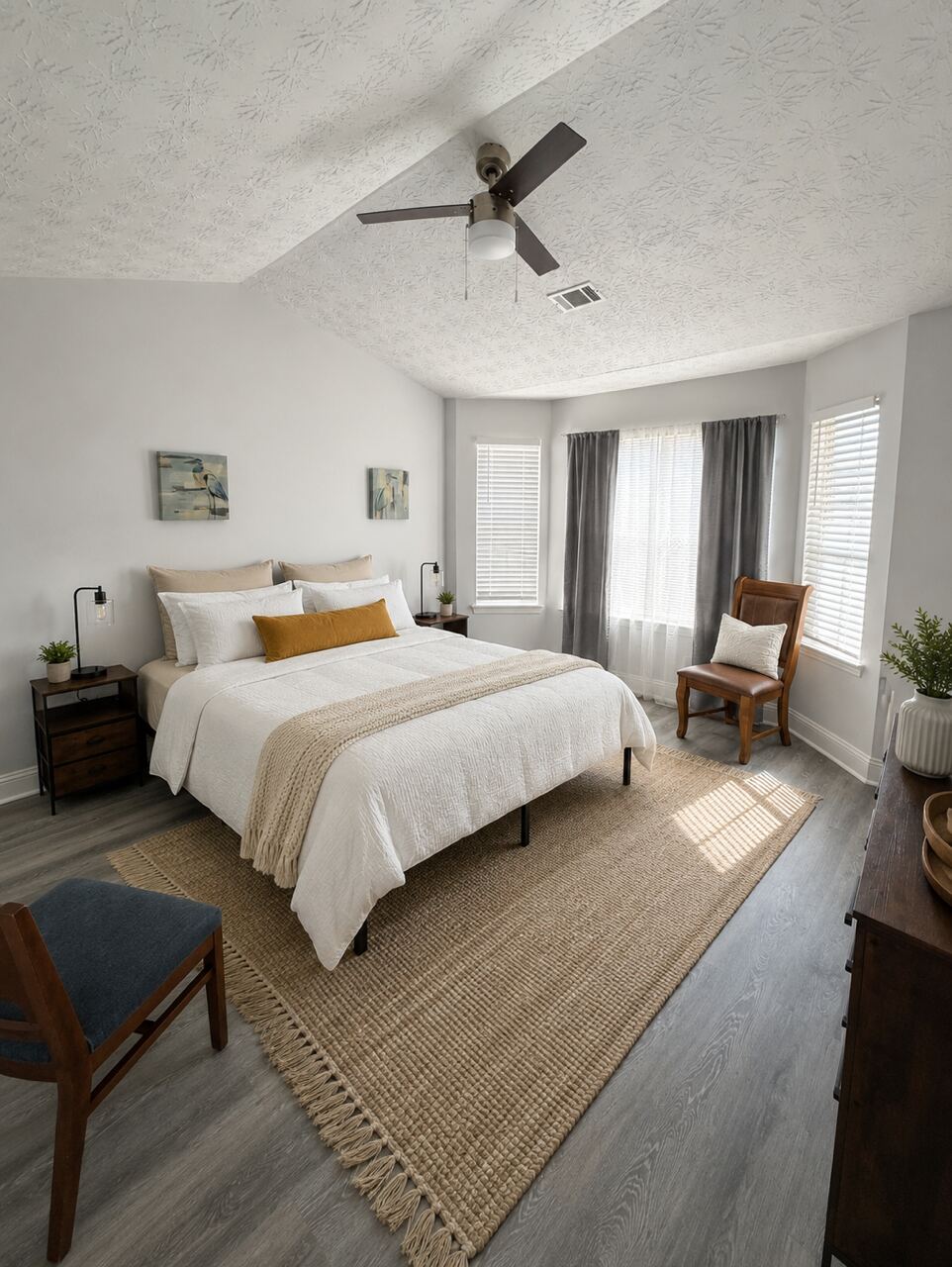 A furnished bedroom with a queen bed and natural light